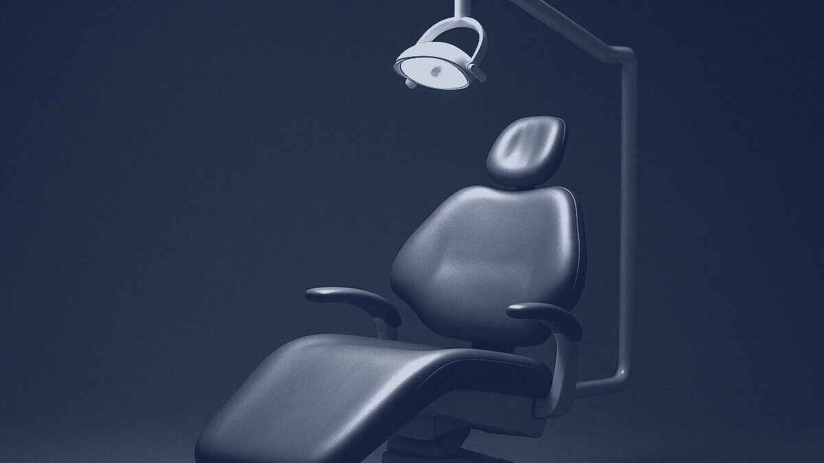 An empty dentist's chair under a single overhead lamp